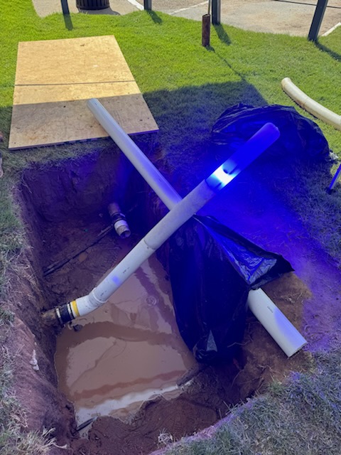Pelican Underground LLC shows how glowing blue pipes signal trenchless pipe repair in progress at a muddy work site.