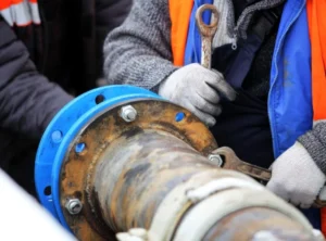 workers show skilled trenchless pipe repair by tightening bolts on a large metal pipe.
