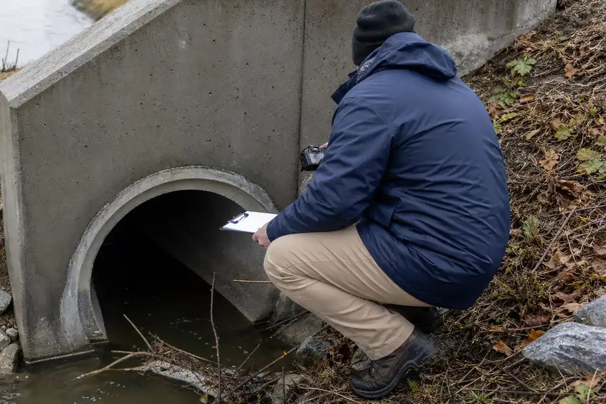 A Pelican Underground LLC worker checks water flow at a drainage pipe, making notes and observations for safety.